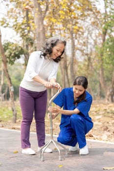 Nurse or female caregiver help senior woman holding stick to walk in the hospital garden