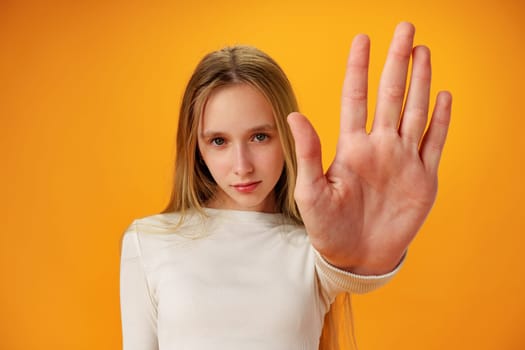 Teen girl extend hand in block gesture against yellow background