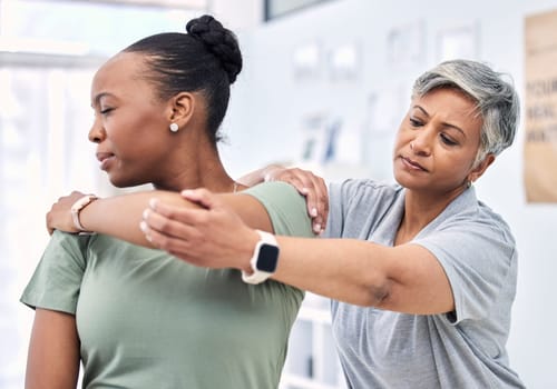 Shoulder pain, physical therapy and chiropractor with patient, injury and healthcare with help and women at clinic. Physiotherapy, stretching muscle and anatomy with body, support and trust in health
