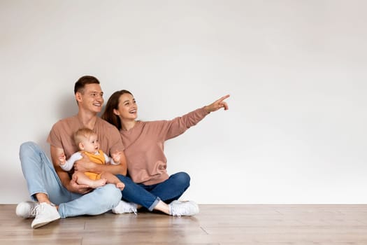Happy Family Of Three With Infant Baby Pointing Aside At Copy Space
