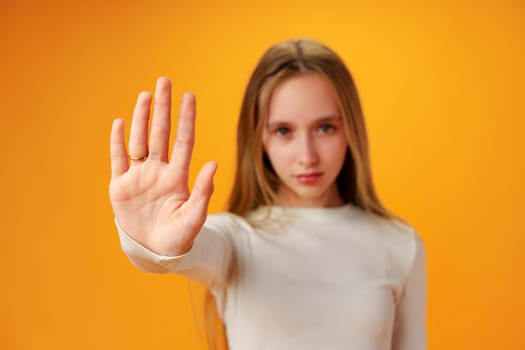 Teen girl extend hand in block gesture against yellow background