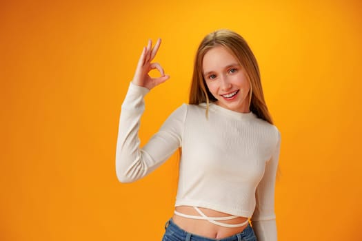 Smiling teen girl showing ok sign against yellow background