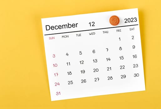The December 2023 and wooden push pin on yellow background.