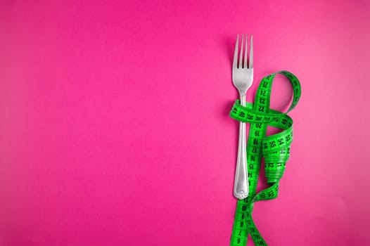 Green tape measure with cutlery on a colored background, top view. Diet and fasting. Weight loss