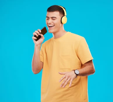 Phone, headphones and man singing in studio listening to music, radio or playlist for entertainment. Smile, technology and male person streaming song or album for karaoke isolated by blue background