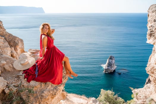 A girl with flowing hair in a long red dress sits on a rock above the sea. The stone can be seen in the sea.