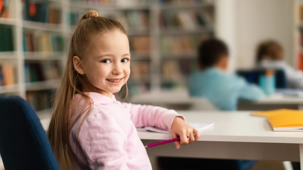 Cheerful european schoolgirl at desk, turning back with a smile