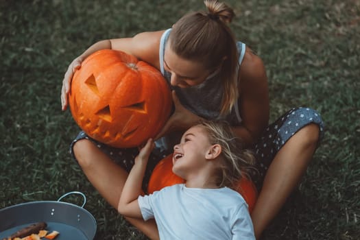 A happy mother and son enjoying Halloween celebration. Holding a frightening pumpkin with an evil expression on it's face, which they made themselves