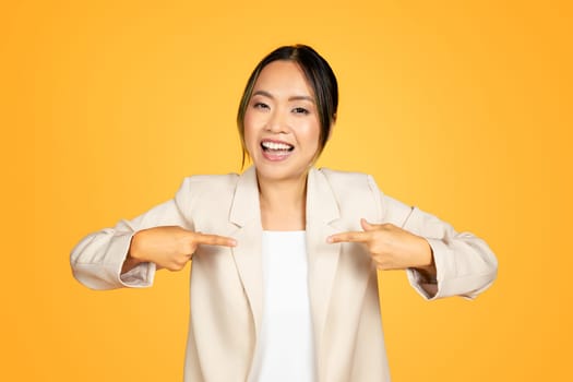 Confident Asian woman pointing finger at herself, self-assured and bold on orange background