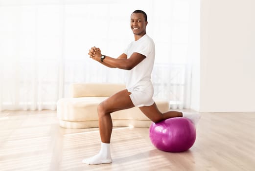 Cheerful young african american sportsman exercising with fitness ball