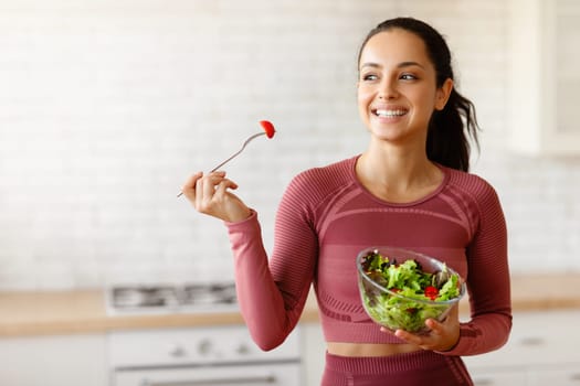 Fitness lady enjoys a vegetable salad in kitchen at home, choosing healthy food and products, holding bowl full of veggies meal. Mindful eating routine, slimming nutrition