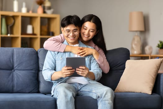 Smiling korean couple websurfing on tablet gadget at home