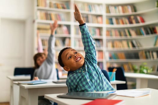 Children at desks raising hands during classroom lesson