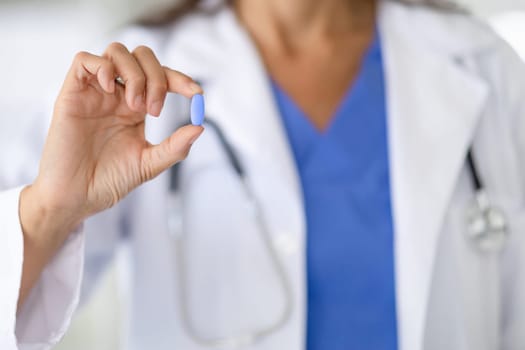 Woman doctor holds one medical pill in her hand close-up