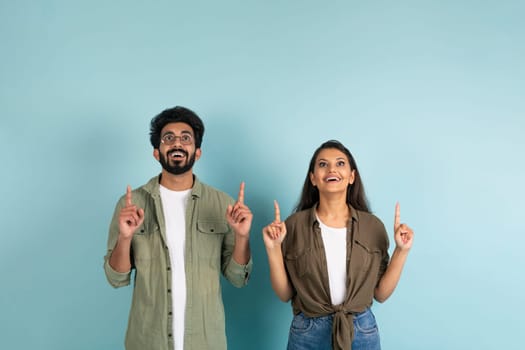 Excited young hindu couple pointing up at copy space