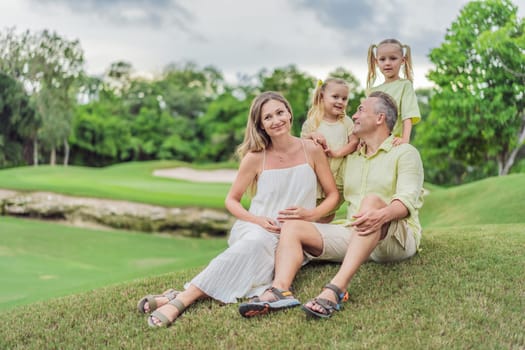 A happy family, two girls, dad, and a pregnant mom, enjoys quality time together on a lush green lawn, creating cherished memories of togetherness