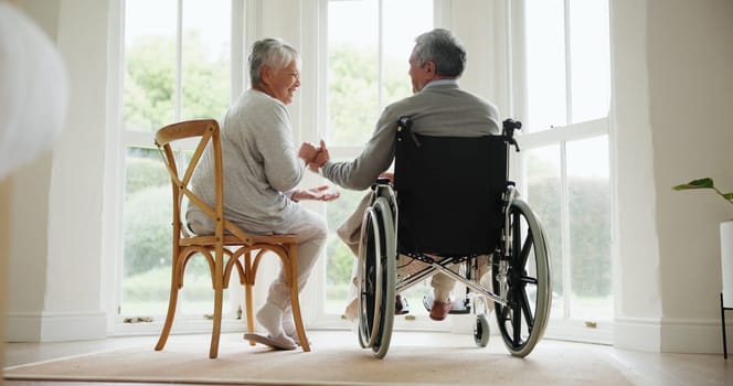 Wheelchair, senior couple and conversation in a retirement and nursing home with support and holding hands. Back, love and man with a disability with speaking and discussion with empathy in marriage