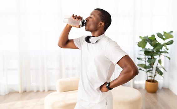 Athletic young black sportsman drinking water, exercising at home