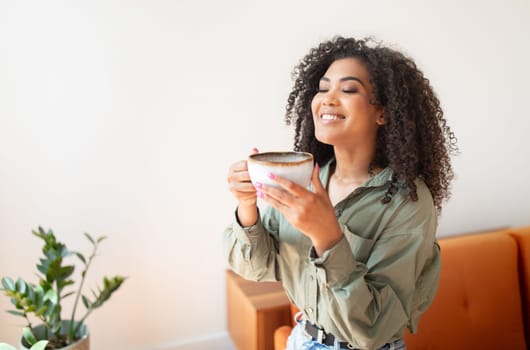 Glad young black lady drinks favorite tea in living room