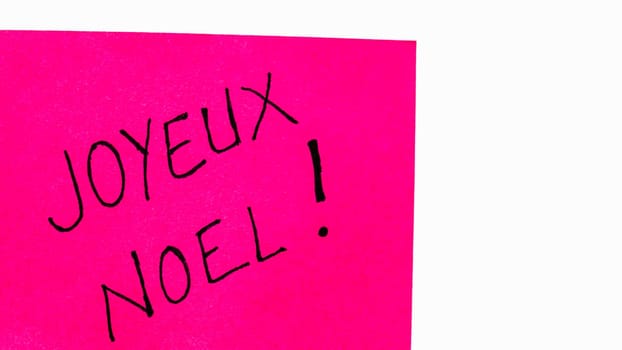 Joyeux noel (Merry Christmas) handwriting text close up isolated on pink paper with copy space. Writing text on memo post reminder