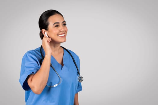 Latin woman doctor with earpad, consulting patient online over grey background, copy space