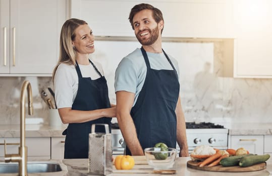 Kitchen, apron and couple with cooking, smile and healthy food with ingredients, bonding and anniversary. Happy people, home and man with woman, recipe and bonding with activity, lunch and vegetables
