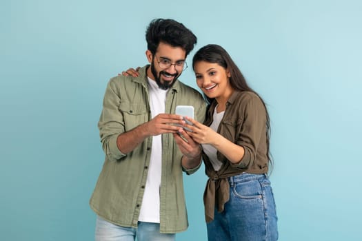 Amazed young indian couple shopping online, using smartphone