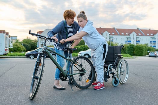 Boy transfers from wheelchair to bicycle, mother helping child to transfer