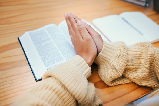 Hands, bible and praying at desk, religion and Christian worship in home at table. Closeup, holy book and woman in meditation for God, Jesus and Christ for faith in spiritual gospel, praise or hope