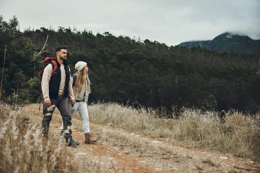 Couple walking, hiking and nature with travel, mountain and backpacking with wilderness and explore outdoor. People holding hands, adventure and holiday with date, environment and trekking path.