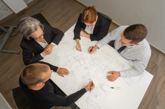 Top view of 4 business people sitting at a table and discussing blueprints. Designers engineers at a meeting.