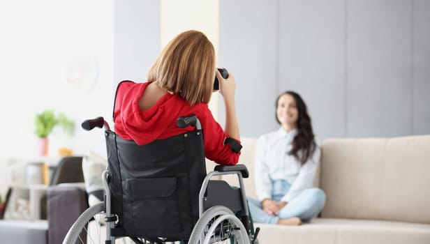 Woman in wheelchair photographs woman on couch