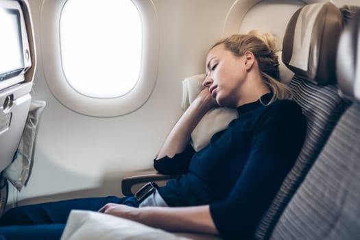 Tired blonde casual caucasian woman napping on airplane.