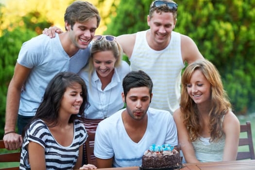 Birthday, friends and blow candles outdoor for celebration, surprise or party with milestone or happiness. Cake, men and women in backyard of home or nature with gathering or social event with smile