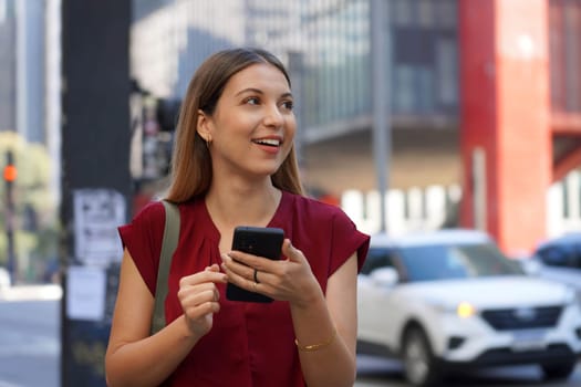 Close-up of attractive Brazilian business woman hail a vehicle using mobile app looking to the side on Paulista Avenue, Sao Paulo, Brazil