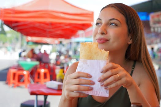 Close-up of Brazilian girl sitting in the fair eating Pastel de Feira stuffed fried pastry 