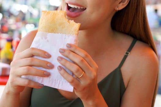 Happy young woman eating Pastel de feira a traditional Brazilian stuffed fried pastry