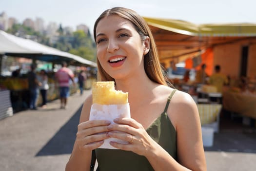 Brazilian woman walks at the fair eating the traditional "pastel" in Sao Paulo, Brazil