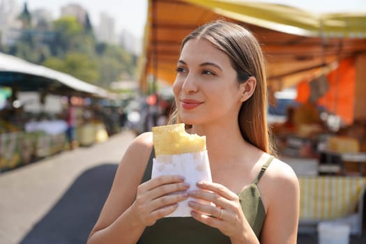 Close-up of beautiful girl eating Brazilian traditional food Pastel de Feira in Sao Paulo, Brazil