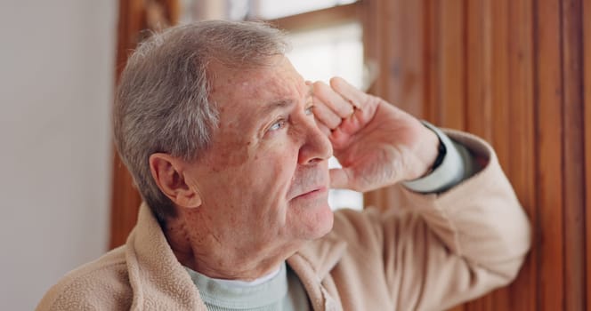 Depression, sad or nostalgia with a senior man looking through a window in his home during retirement. Thinking, memory or the past with an elderly person feeling lonely in the living room of a house
