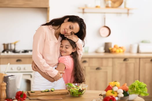 Mom and daughter kid sharing embrace cooking in modern kitchen