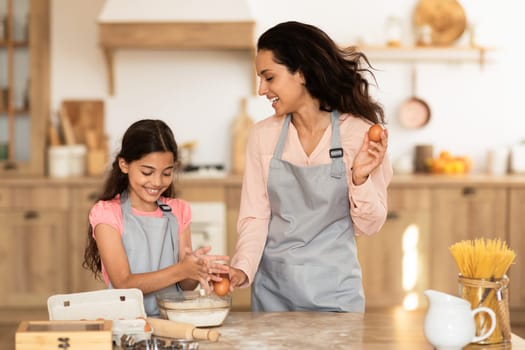 Smiling mom and her daughter preparing cookies dough at kitchen