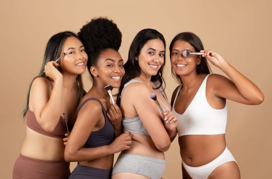 Diverse women, smiling with makeup brushes, studio