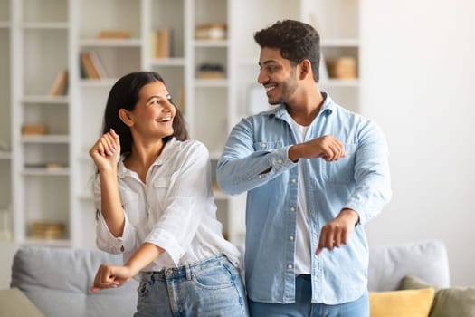 Joyful young indian couple dancing together in living room
