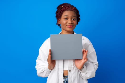 Smiling afro woman showing blank gray paper against blue background