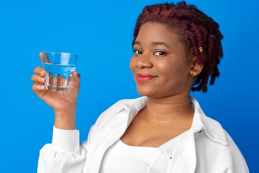 Young african woman drinking water from a glass against blue background