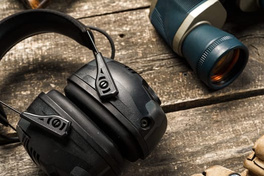 Protective headphones and binoculars on wooden background