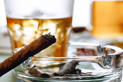 Close up of smoking cigar and whiskey glass on table