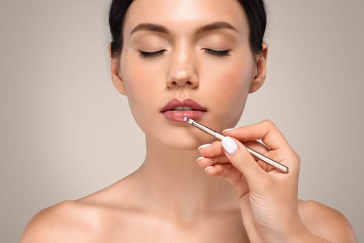 Calm millennial caucasian woman enjoy makeup, hand of professional visagiste apply lipstick on lips