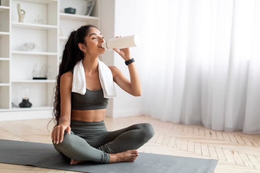 Fit lady sitting on sports mat with bottle of water
